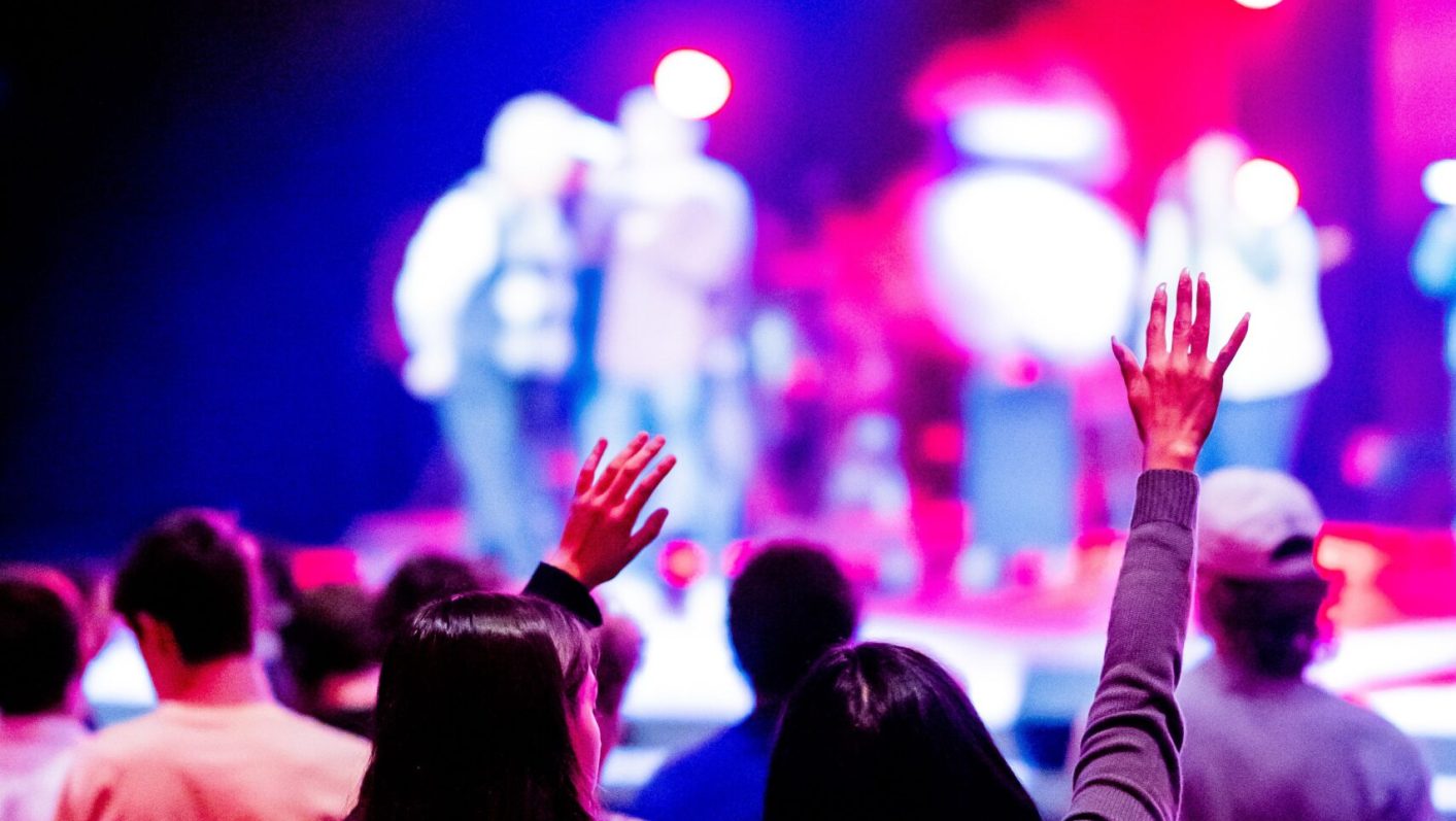 Energetic concert scene with audience members raising their hands under vibrant lighting.